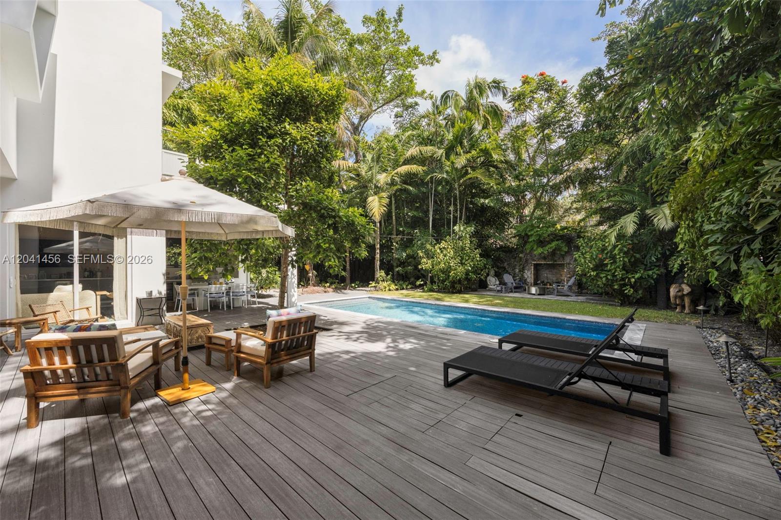 A wooden deck features a swimming pool, lounge chairs, and an umbrella in a backyard — 3901 Kumquat Ave, Miami FL 33133, MIAMI, FL