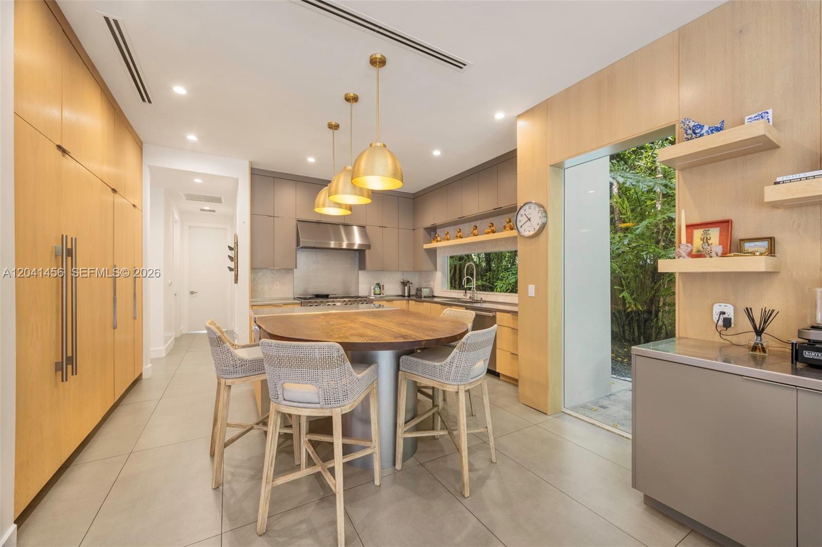 A modern kitchen features a round wooden island, bar stools, and light wood cabinetry — 3901 Kumquat Ave, Miami FL 33133, MIAMI, FL