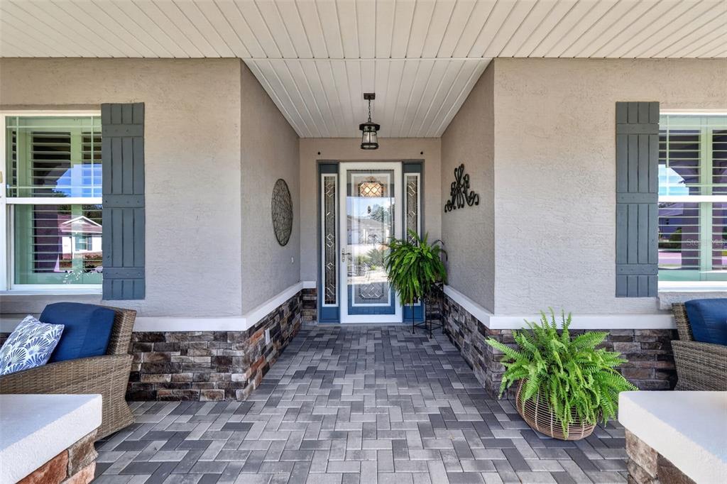 A covered front porch features stone veneer accents, gray pavers, and a glass-paneled front door — 9133 SW 82ND LANE, OCALA, FL