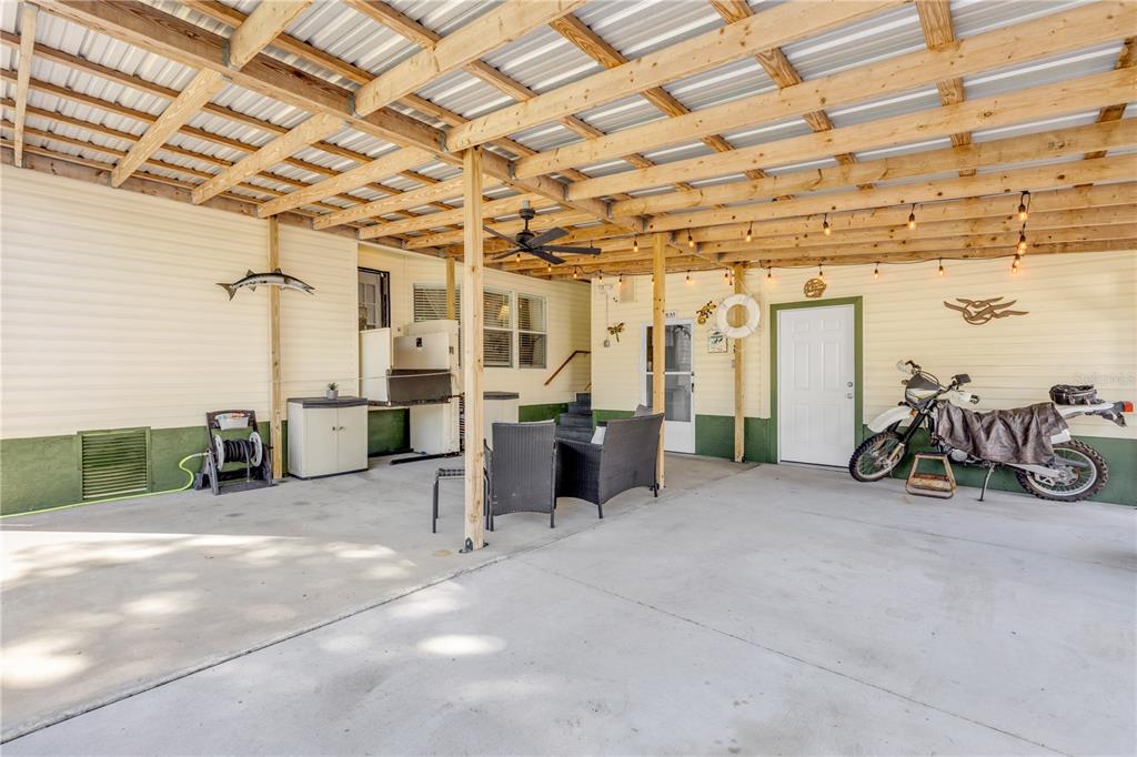 A covered concrete patio features a ceiling fan, string lights, outdoor furniture, and a motorcycle — 530 MILL RUN DRIVE, NEW SMYRNA BEACH, FL