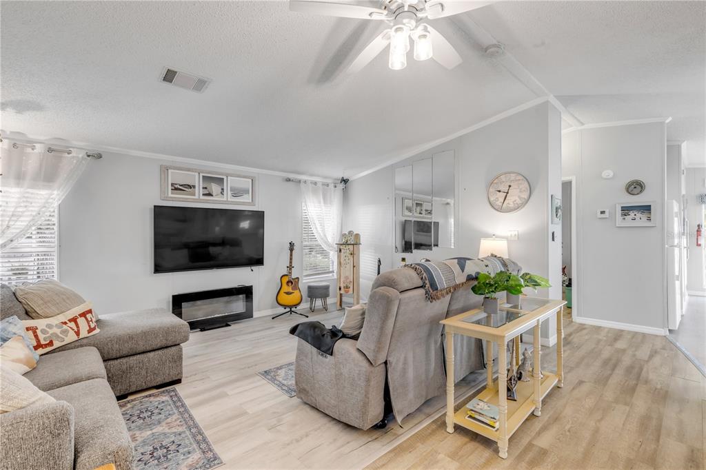 A living room features light wood flooring, a grey sectional sofa, and a wall-mounted television — 530 MILL RUN DRIVE, NEW SMYRNA BEACH, FL