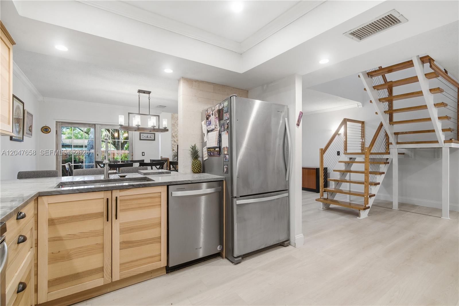 A kitchen with light wood cabinets and stainless steel appliances sits beside an open staircase — 2822 N 34th Ave, Hollywood FL 33021, HOLLYWOOD, FL