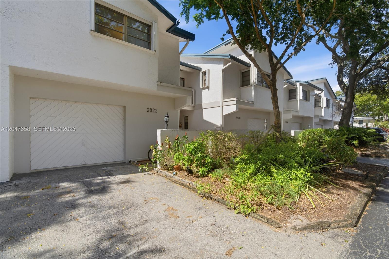 A row of multi-story townhouses features white stucco exteriors, attached garages, and a landscaped front yard — 2822 N 34th Ave, Hollywood FL 33021, HOLLYWOOD, FL