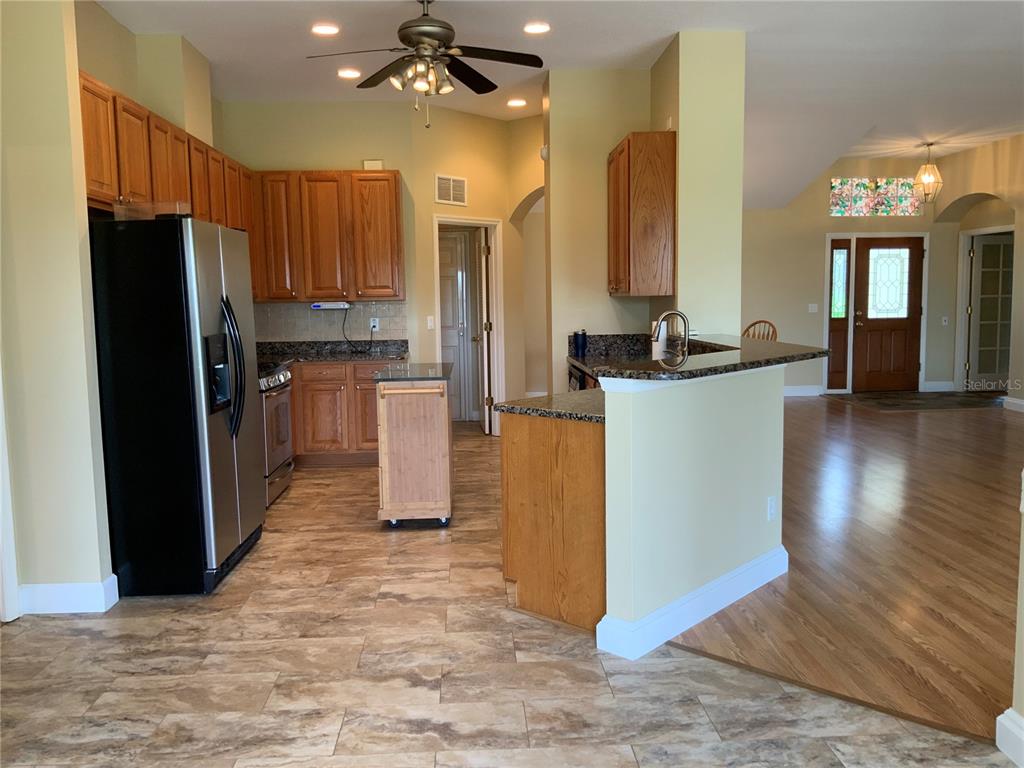 A kitchen with wood cabinets, stainless steel appliances, and a breakfast bar overlooks a foyer — 5475 BOUNTY CIRCLE, TAVARES, FL