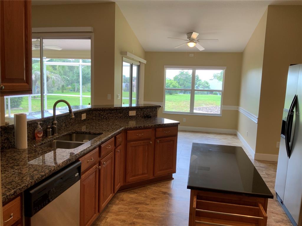 A kitchen features wood cabinets, granite countertops, a center island, and views of the backyard — 5475 BOUNTY CIRCLE, TAVARES, FL