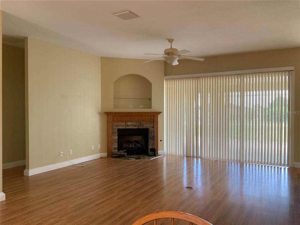 A living room with wood-look flooring, a stone fireplace, and vertical blinds covering sliding doors — 5475 BOUNTY CIRCLE, TAVARES, FL