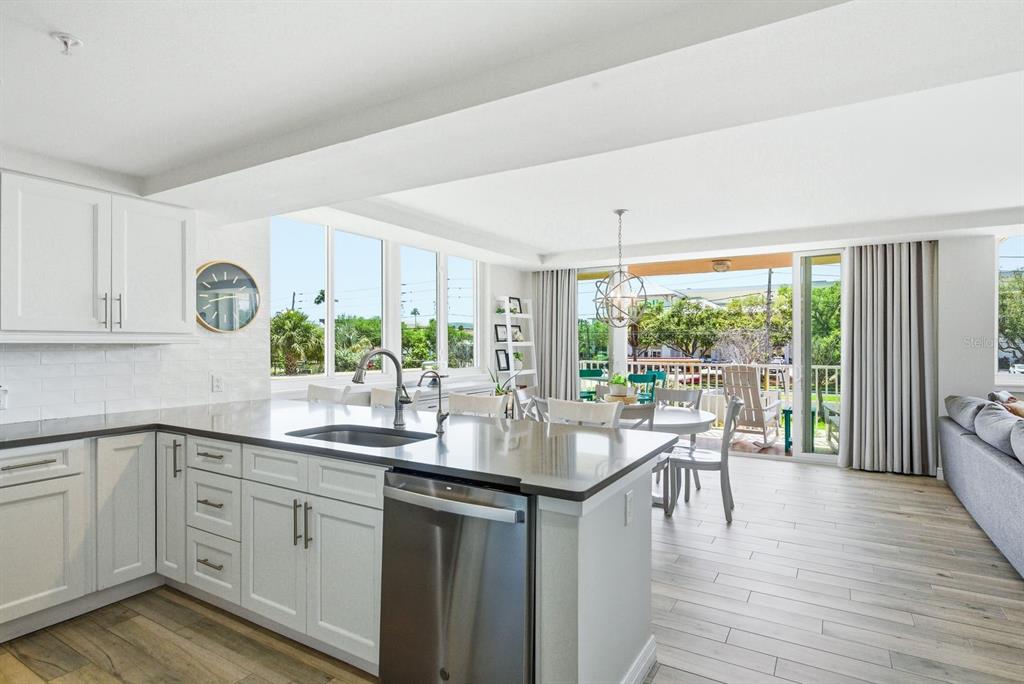 A modern kitchen with white cabinets and stainless steel appliances overlooks a bright dining area — 223 ISLAND WAY UNIT 2D, CLEARWATER BEACH, FL