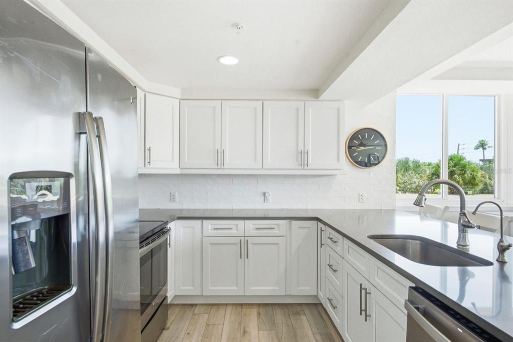 A kitchen features white cabinets, stainless steel appliances, gray countertops, and a window with greenery — 223 ISLAND WAY UNIT 2D, CLEARWATER BEACH, FL