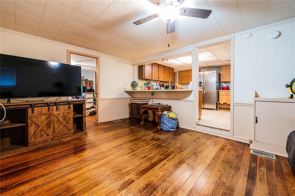 A living room with wood flooring, a television console, and an open kitchen pass-through — 5140 LAKELAND HIGHLANDS ROAD, LAKELAND, FL