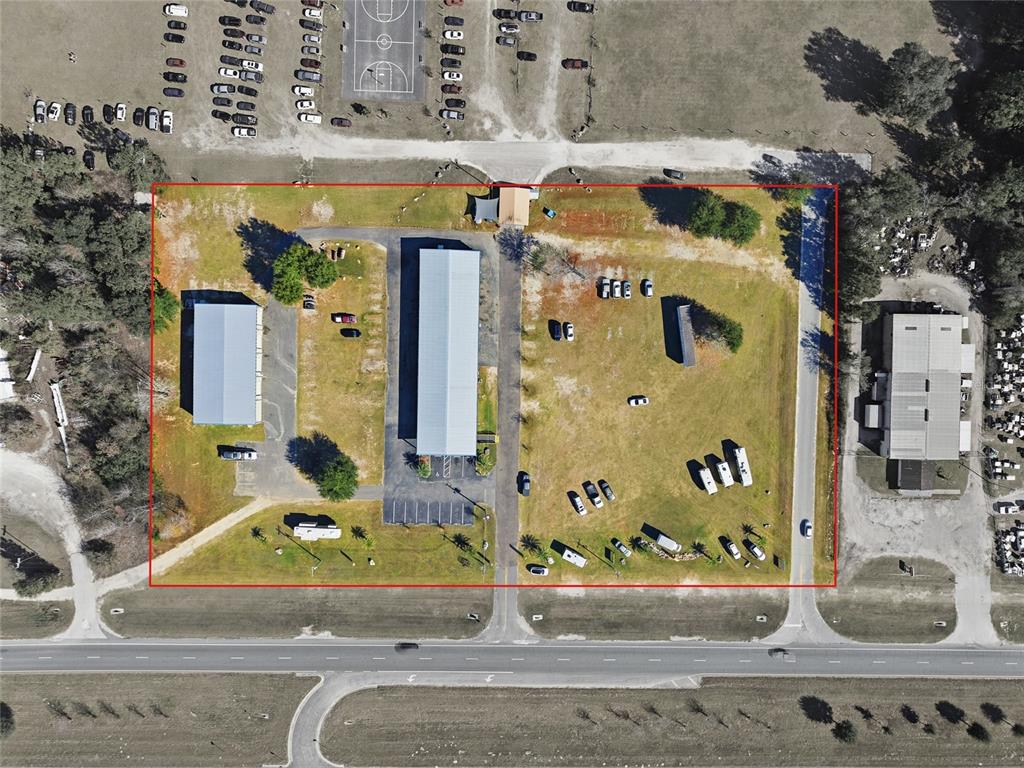 This aerial view shows a commercial property with two buildings, parking areas, and grassy grounds — 20761 NE HIGHWAY 27, WILLISTON, FL