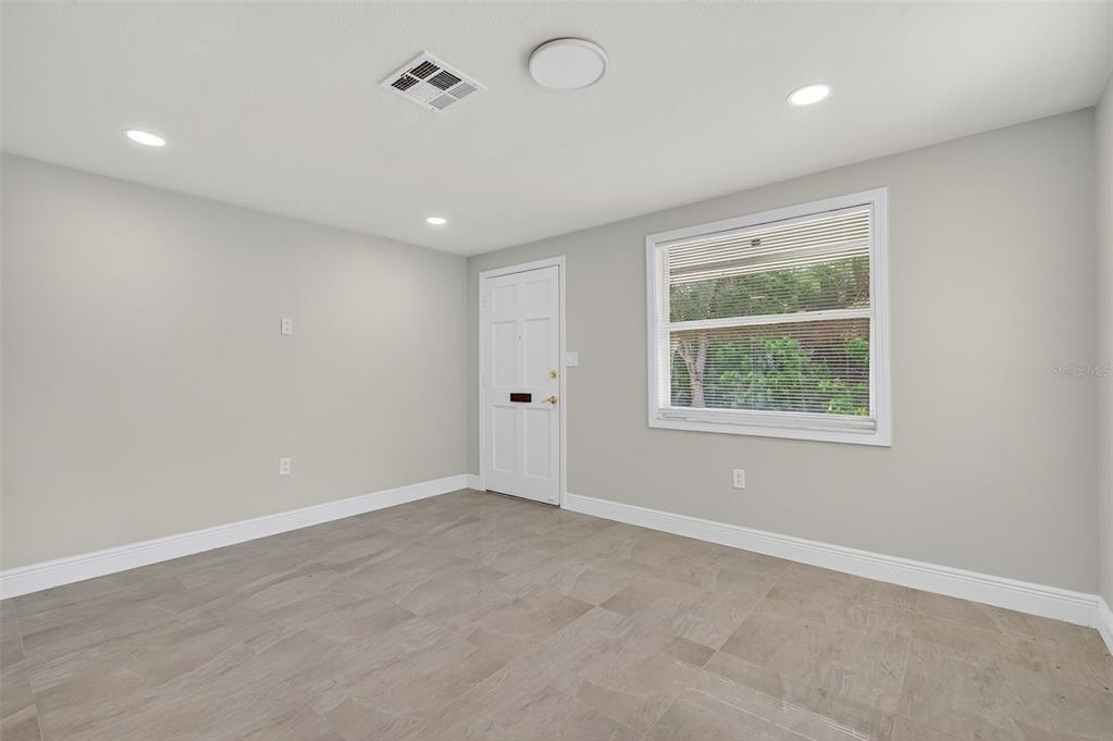 An empty room features light gray walls, tile flooring, a white door, and a window — 4929 DOCNER STREET, NEW PORT RICHEY, FL