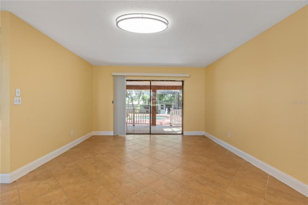 An empty room with yellow walls, tile flooring, and sliding glass doors leading to a pool — 7369 TARRYTOWN DRIVE, SPRING HILL, FL