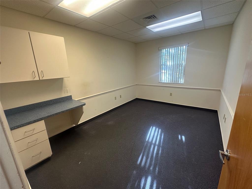 An empty office features a blue countertop, white cabinets, dark carpeting, and a window — 4611 NW 53RD AVENUE UNIT A, GAINESVILLE, FL