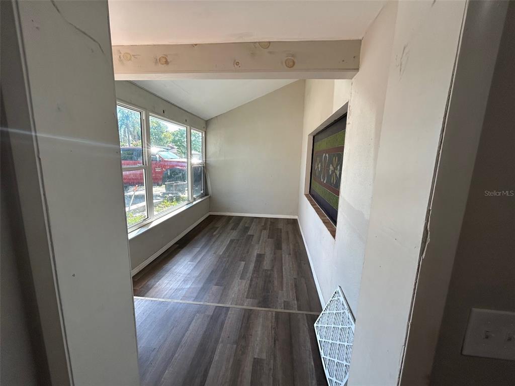 A sunroom with wood-look flooring, large windows, and a sloped ceiling viewed through a doorway — 7403 FOXBLOOM DRIVE, PORT RICHEY, FL