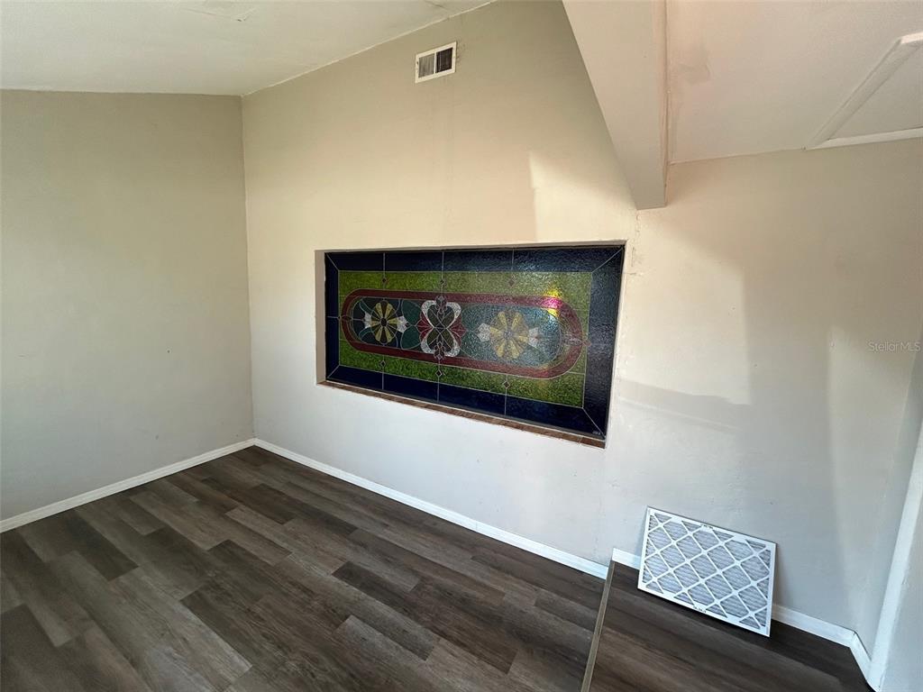 A room with wood-look flooring features a rectangular stained-glass window inset into the wall — 7403 FOXBLOOM DRIVE, PORT RICHEY, FL