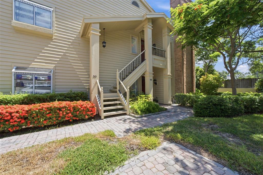 A two-story tan building features an exterior staircase leading to an upper-level entrance — 50 PELICAN PLACE UNIT 50, CLEARWATER, FL