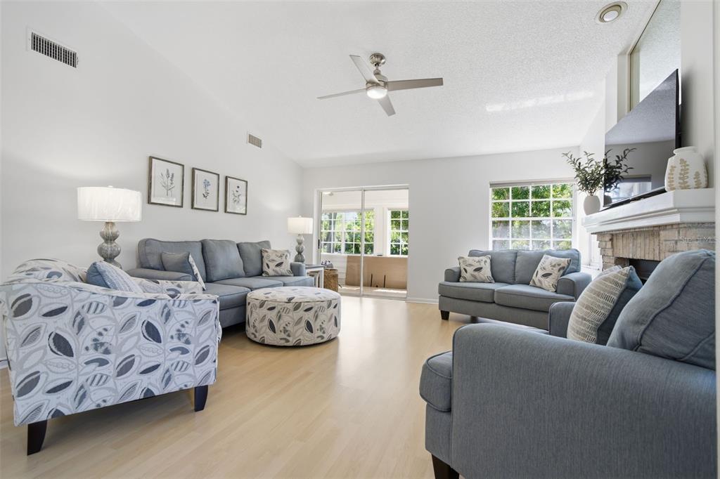 A bright living room features light wood flooring, blue sofas, and a brick fireplace — 50 PELICAN PLACE UNIT 50, CLEARWATER, FL