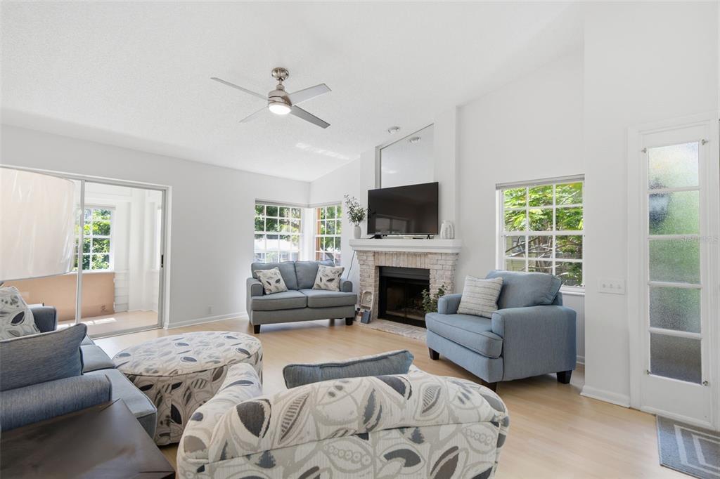 A living room features a brick fireplace, blue furniture, light wood floors, and sliding doors — 50 PELICAN PLACE UNIT 50, CLEARWATER, FL