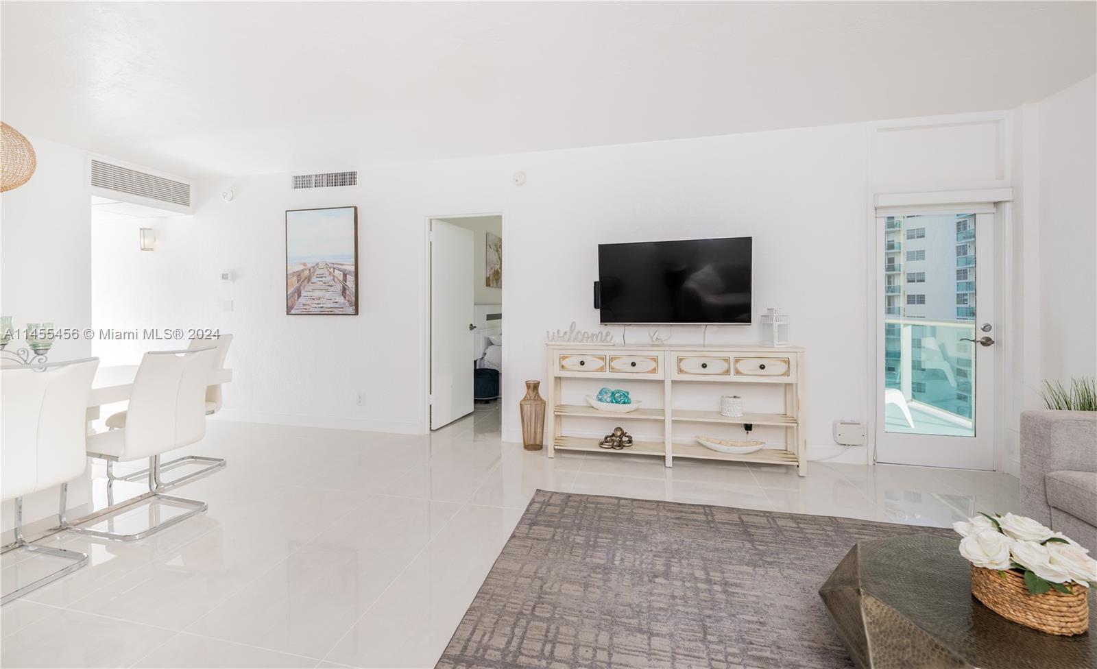 A bright living room features white tile floors, a television console, and a balcony door — 3801 S Ocean Dr # 7O, Hollywood FL 33019, HOLLYWOOD, FL