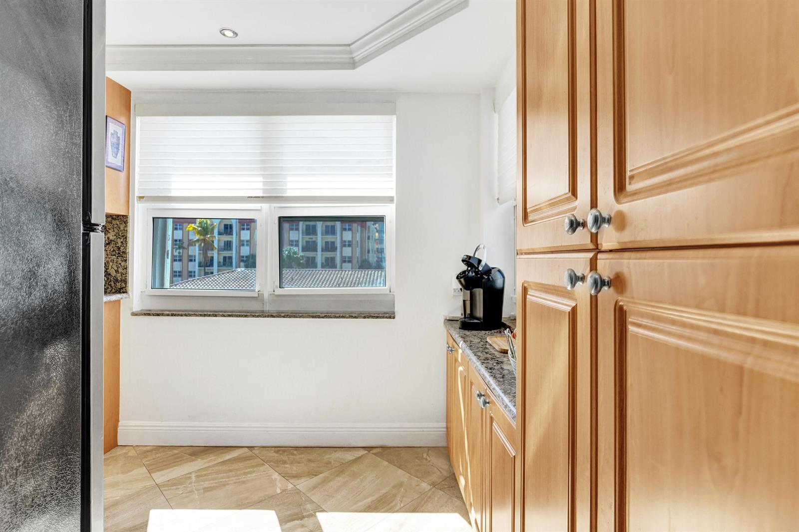 A kitchen features light wood cabinets, granite countertops, tile flooring, and a window with blinds — 405 N Ocean Boulevard # 229, Pompano Beach FL 33062, POMPANO BEACH, FL