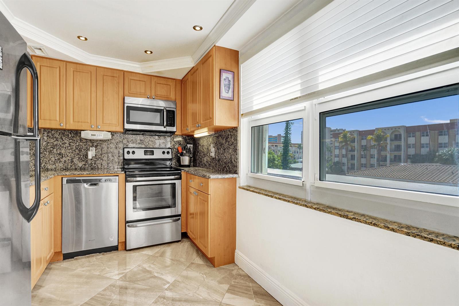 A kitchen with light wood cabinets, granite countertops, stainless steel appliances, and a large window — 405 N Ocean Boulevard # 229, Pompano Beach FL 33062, POMPANO BEACH, FL