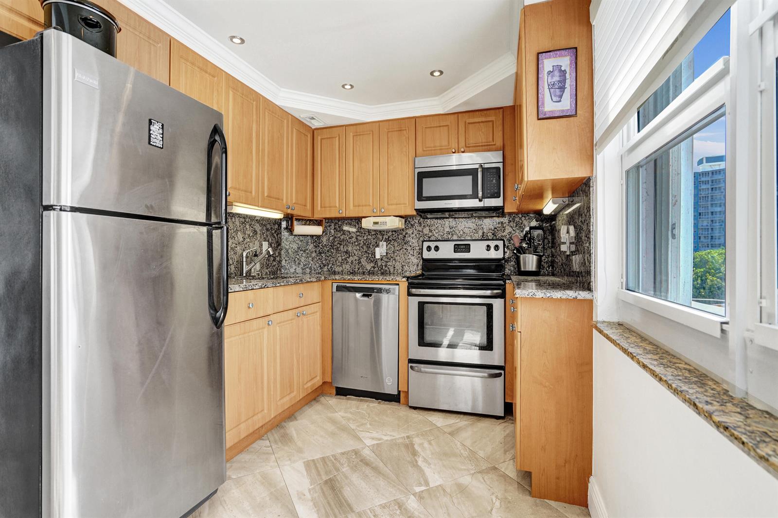 A kitchen with light wood cabinets, granite countertops, stainless steel appliances, and tile flooring — 405 N Ocean Boulevard # 229, Pompano Beach FL 33062, POMPANO BEACH, FL