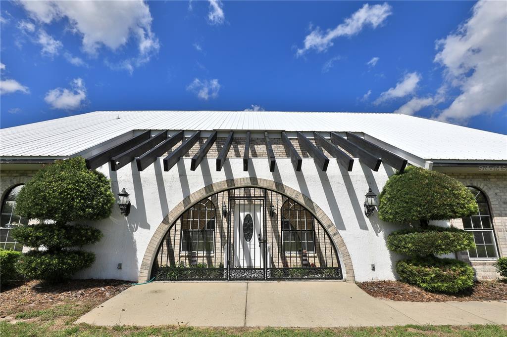 The exterior of a house features a white metal roof, stucco walls, and a gated entryway — 4450 SE 216TH AVENUE UNIT Option 2, MORRISTON, FL