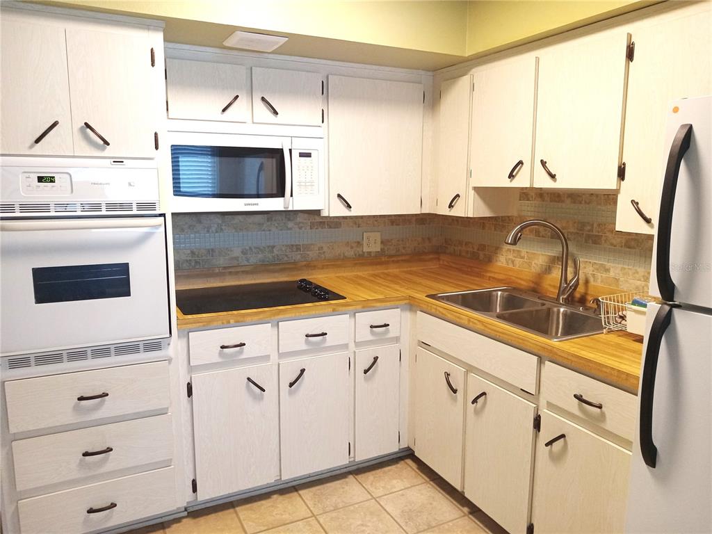 A kitchen with white cabinets, wood countertops, a double sink, and white appliances — 2430 FLORENTINE WAY UNIT 30, CLEARWATER, FL