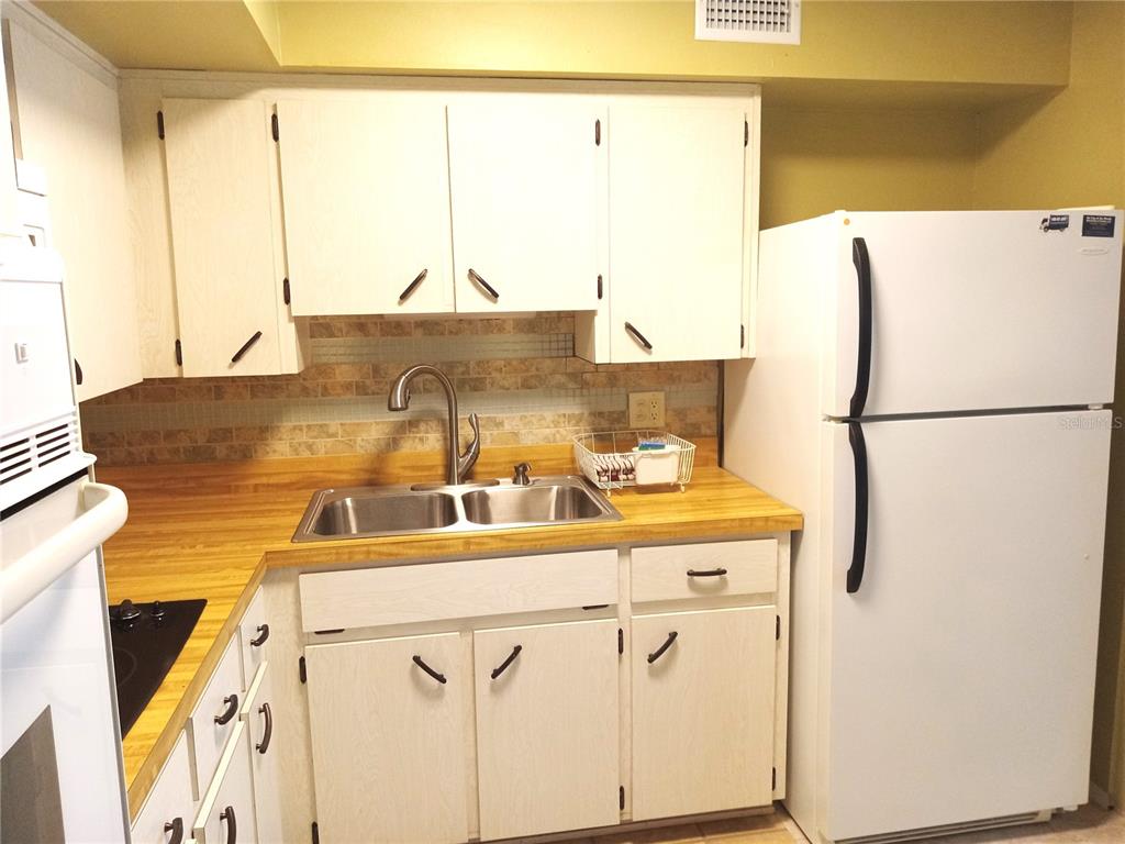 A kitchen features white cabinets, a wood-look laminate countertop, a double sink, and white appliances — 2430 FLORENTINE WAY UNIT 30, CLEARWATER, FL