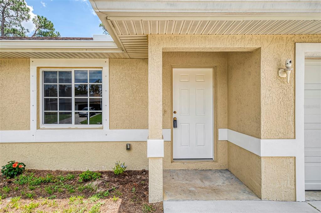 The exterior of a house features a white front door, a window, and stucco siding — 4845 HADER ROAD, NORTH PORT, FL