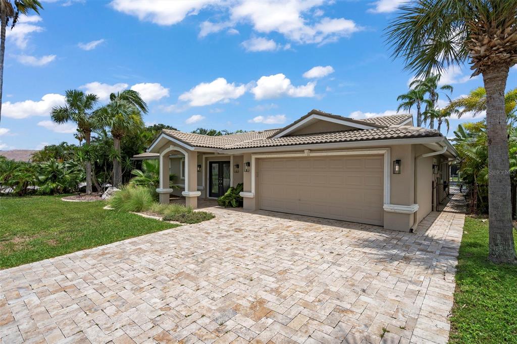 A single-story house with a beige stucco exterior, a tiled roof, and a stone paver driveway — 5548 LEEWARD LANE, NEW PORT RICHEY, FL