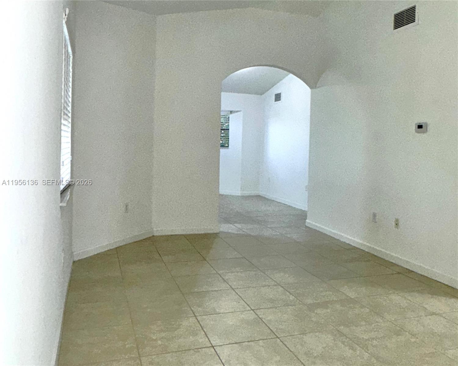 An empty room with beige tile flooring features an arched entryway leading to another space — 22441 SW 88th Pl # 5, Cutler Bay FL 33190, CUTLER BAY, FL