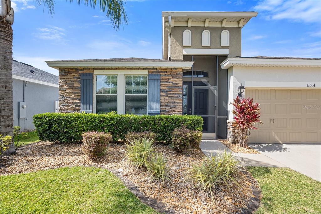 The exterior of a single-story house features a stone facade, a screened entryway, and landscaping — 11504 HARLAN EDDY COURT, RIVERVIEW, FL