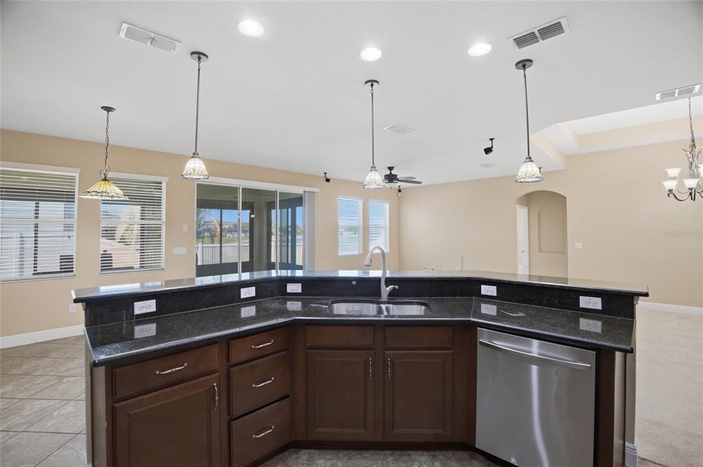 A kitchen island with dark wood cabinets and granite countertops faces a bright living area — 11504 HARLAN EDDY COURT, RIVERVIEW, FL