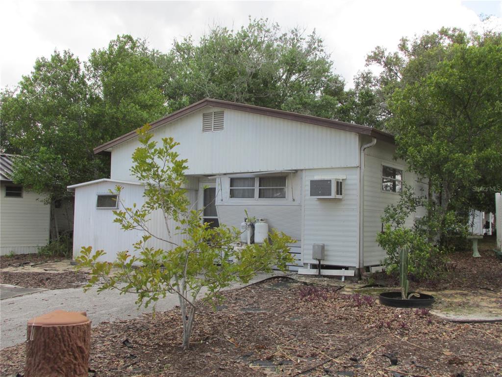 A white single-story mobile home with a metal roof sits on a wooded lot — 13 SADDLEBAG TRAIL S, LAKE WALES, FL