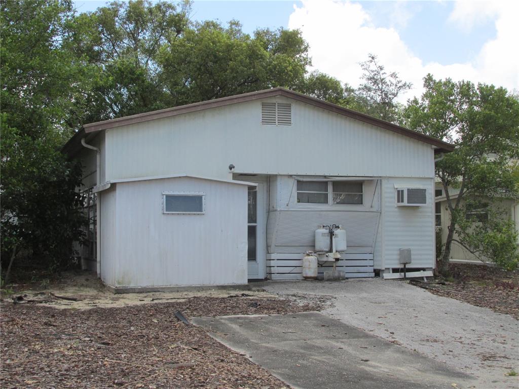 A single-story mobile home with white metal siding, a small shed, and propane tanks — 13 SADDLEBAG TRAIL S, LAKE WALES, FL