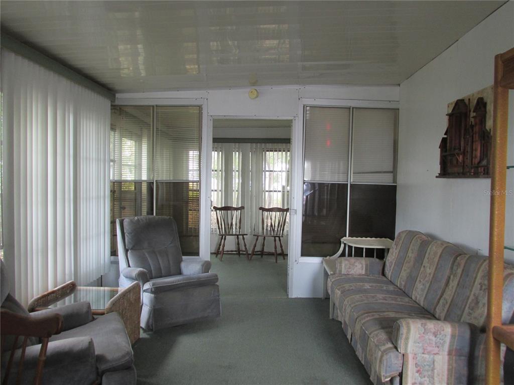 A sunroom features a striped sofa, a recliner, and large windows with vertical blinds — 13 SADDLEBAG TRAIL S, LAKE WALES, FL