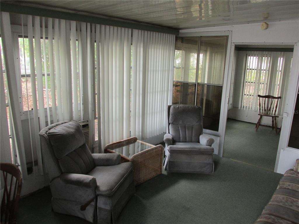 A sunroom features two gray recliners, a wicker side table, and vertical blinds on windows — 13 SADDLEBAG TRAIL S, LAKE WALES, FL