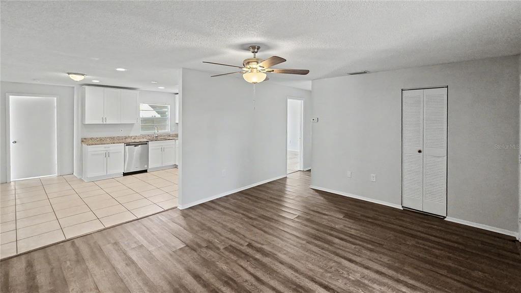 An empty living room features light gray walls, wood-look flooring, a large window, and sliding doors — 7419 IVORY TERRACE, NEW PORT RICHEY, FL