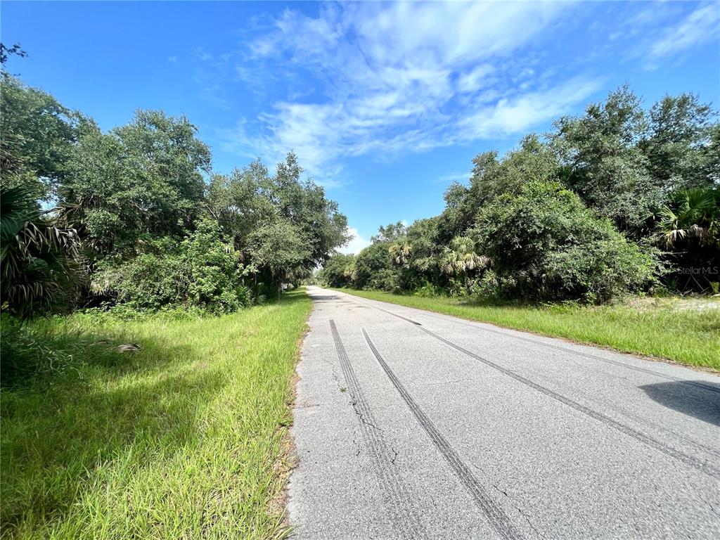 A paved road stretches through a wooded area under a blue sky with clouds — 19136 RUSKIN AVENUE, PORT CHARLOTTE, FL