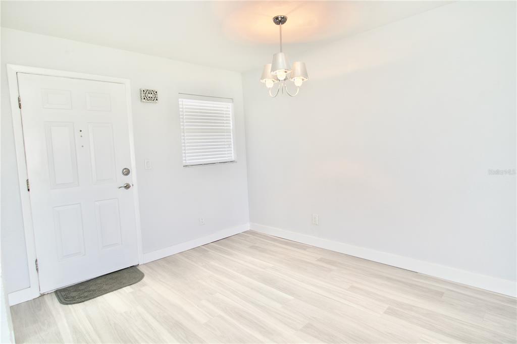 A bright room with light wood-look flooring, a white door, and a modern chandelier — 5135 GEMSTONE DRIVE UNIT 202, NEW PORT RICHEY, FL