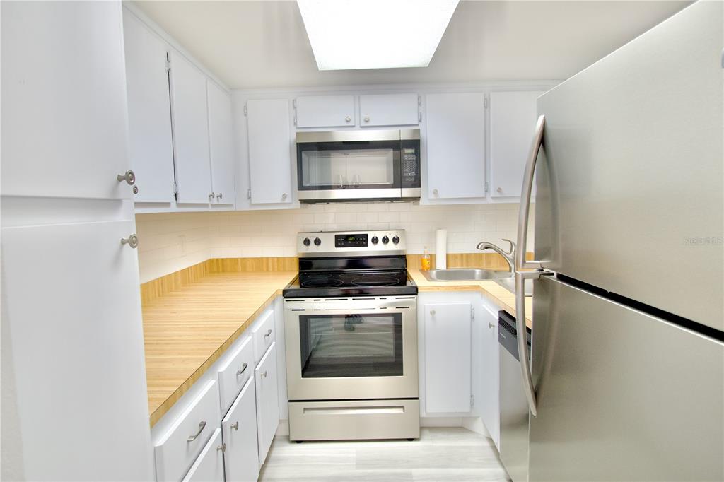 A galley kitchen features white cabinets, stainless steel appliances, and light wood-look countertops — 5135 GEMSTONE DRIVE UNIT 202, NEW PORT RICHEY, FL