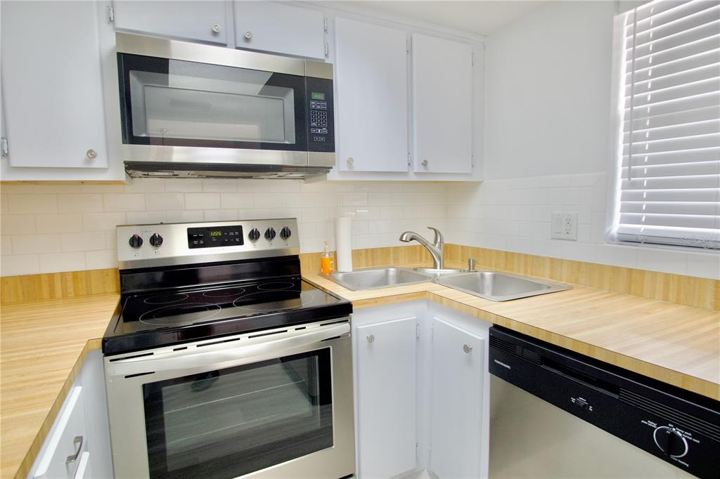 A kitchen features white cabinets, stainless steel appliances, a double sink, and wood-look countertops — 5135 GEMSTONE DRIVE UNIT 202, NEW PORT RICHEY, FL