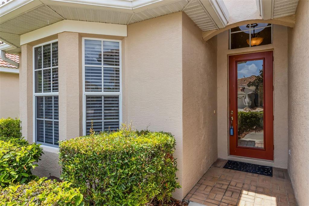 The exterior of a home features a red front door, a bay window, and landscaping — 6348 ROOKERY CIRCLE, BRADENTON, FL