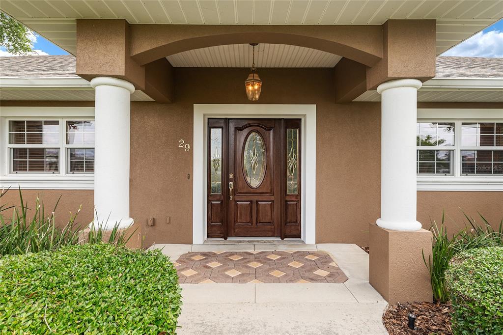 The front exterior of a house features a brown facade, white columns, and a wooden door — 29 SE OCALE WAY, SUMMERFIELD, FL