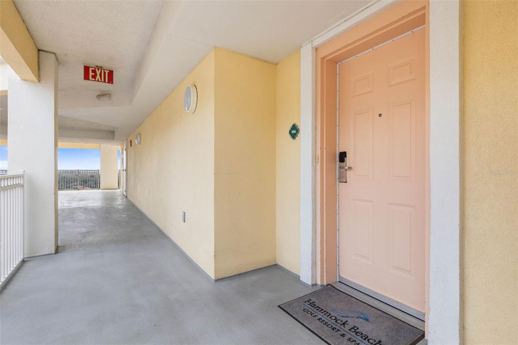 A peach-colored door with a resort doormat sits on a concrete outdoor hallway — 200 OCEAN CREST DRIVE UNIT 906, PALM COAST, FL