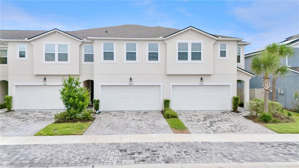 A row of three-story townhomes with white stucco facades, two-car garages, and paver driveways — 19431 MONARCH WIND WAY, LUTZ, FL