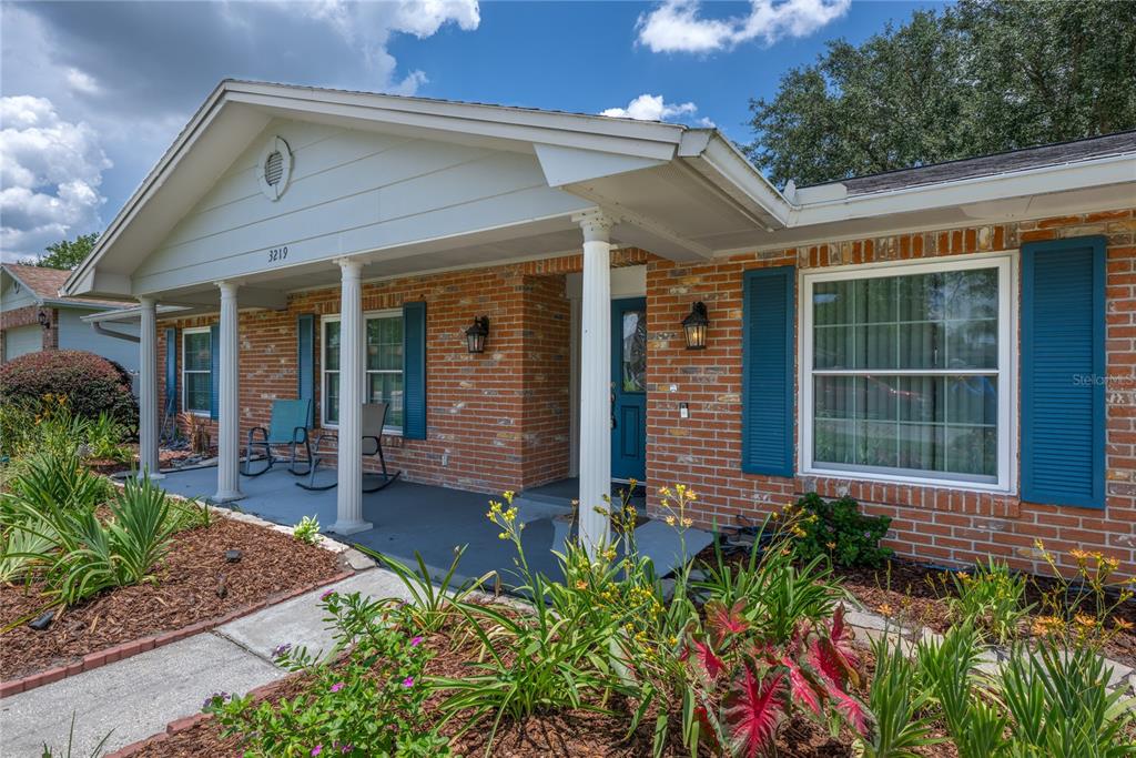 A brick house exterior features a covered front porch with white columns and blue shutters — 3219 HIDALGO DRIVE, ORLANDO, FL