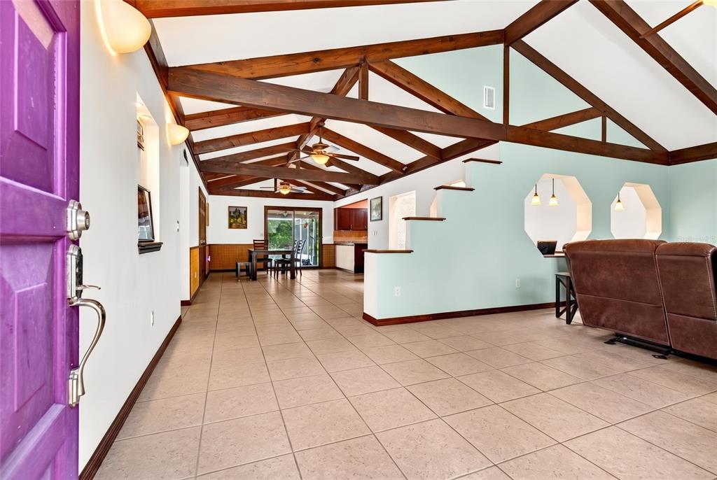 A spacious room features vaulted ceilings with exposed wooden beams and light-colored tile flooring — 10848 N DRAGONIS DRIVE, DUNNELLON, FL