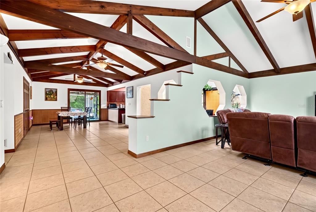 A living room with vaulted ceilings, exposed wood beams, tile floors, and a staircase — 10848 N DRAGONIS DRIVE, DUNNELLON, FL
